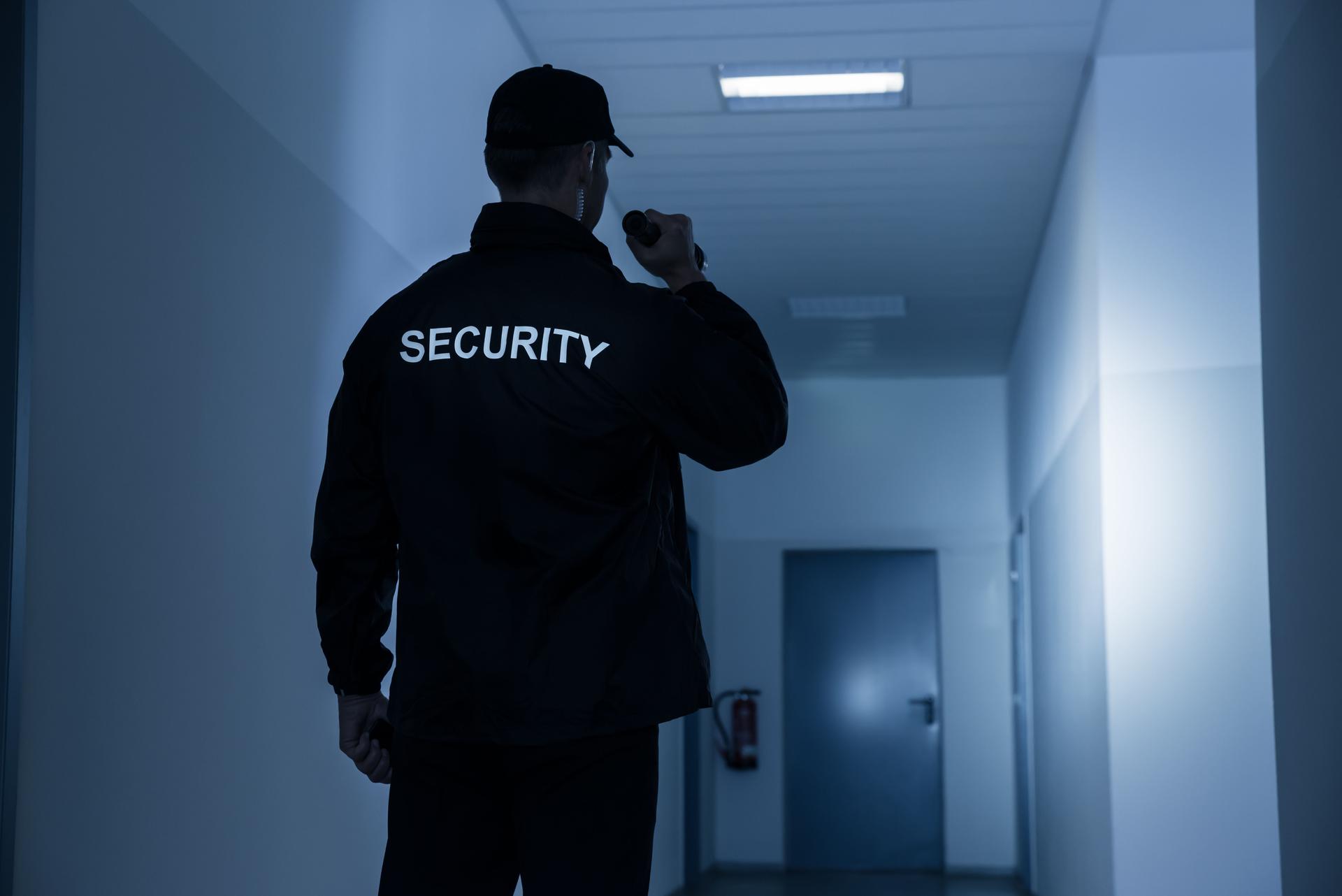 Security Guard With Flashlight In Building Corridor