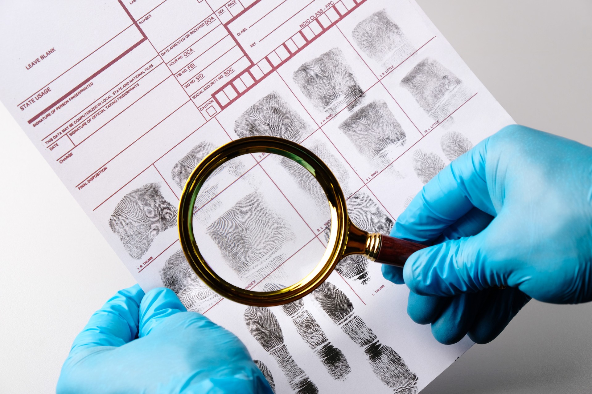 Forensic expert criminologist examines fingerprint card with magnifying glass, holds in gloved hands close-up, fingerprint examination